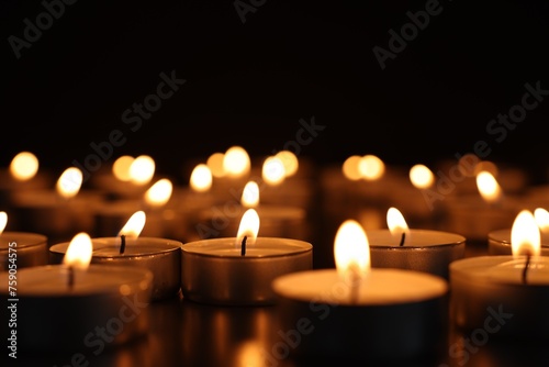 Burning candles on dark surface against black background, closeup