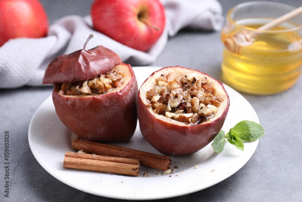 Tasty baked apples with nuts, honey, cinnamon sticks and mint on gray table, closeup Tasty baked apples with nuts, honey, cinnamon sticks and mint on gray table, closeup