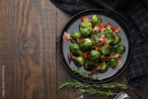 Delicious roasted Brussels sprouts, bacon and rosemary on wooden table, top view. Space for text