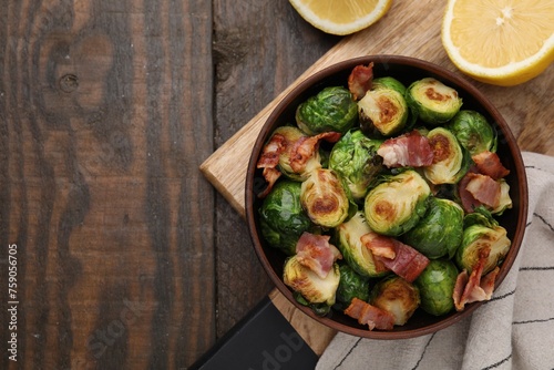 Delicious roasted Brussels sprouts, bacon and lemon on wooden table, top view. Space for text