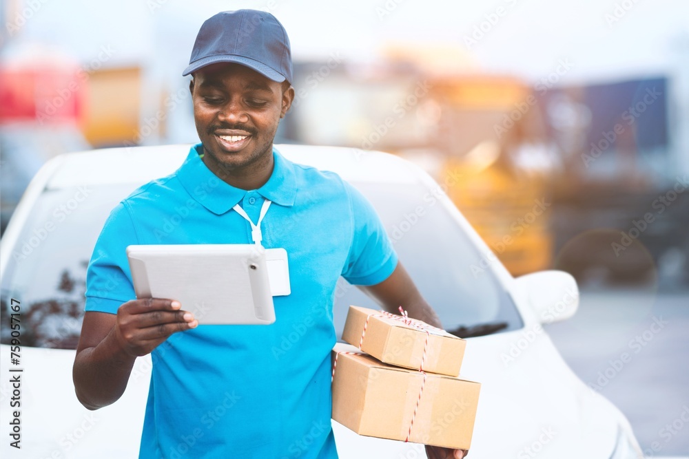 African delivery worker wearing a hat and uniform views delivery information using a tablet African delivery worker wearing a hat and uniform views delivery information using a tablet