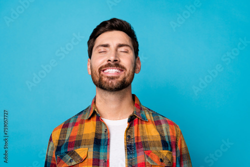Portrait of optimistic dreamy positive guy with stubble wear plaid shirt smiling close eyes relaxing isolated on blue color background photo