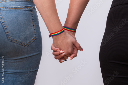 Back view of young lesbian couple in casual clothes, holding hands with nice manicure and rainbow bracelets. Concept of LGTBI pride and LGTBI rights