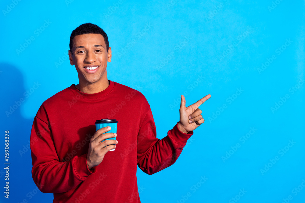 Portrait of positive friendly guy hold coffee cup indicate finger empty space isolated on blue color background