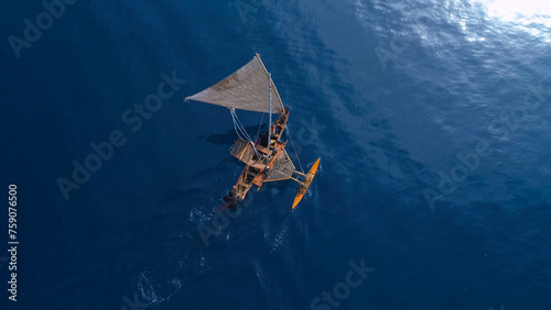 Aerial shot of a traditional Micronesian outrigger sailing canoe surrounded by blue water