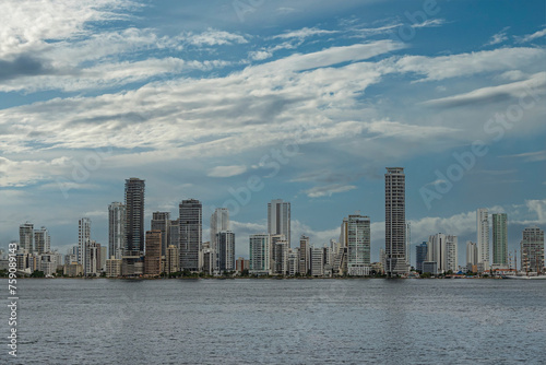 Cartagena, Colombia - July 25, 2023: Long section of east shore with apartment buildings at Bocagrande Neighborhood under blue cloudscape. Tall ship docked at Naval Base  photo