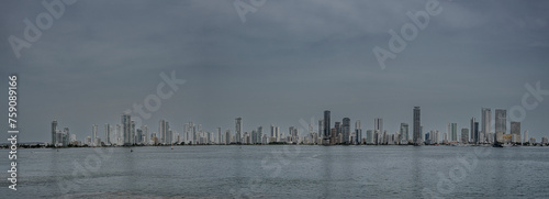 Cartagena, Colombia - July 25, 2023: Panorama, S to N,  east shore with apartment buildings of Bocagrande Neighborhood under dark sky. Tall ships docked at Naval Base  photo