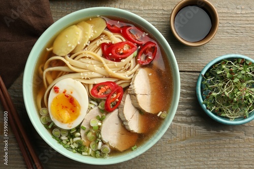 Delicious ramen in bowl, soy sauce and microgreens on wooden table, flat lay. Noodle soup