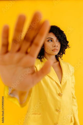 Stylish woman showing stop sign in yellow studio
