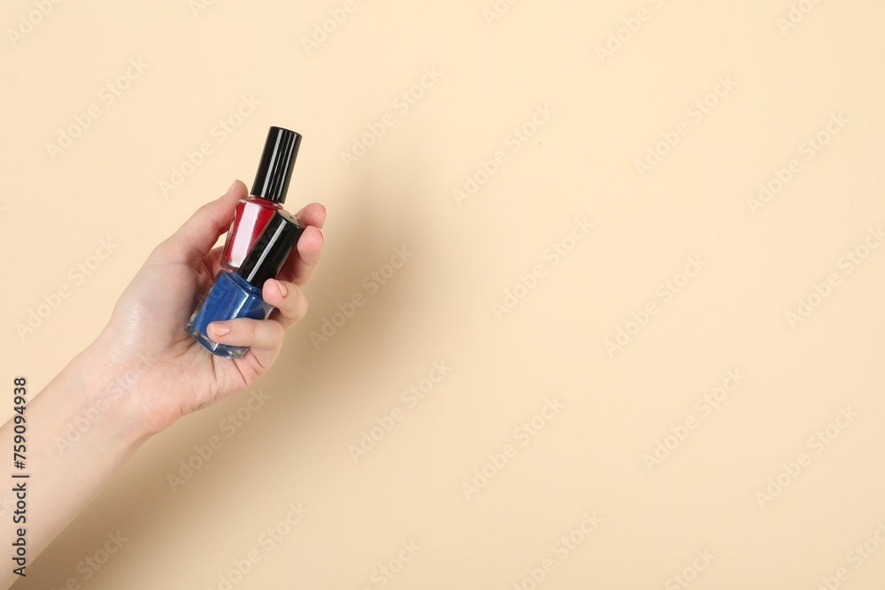Woman holding nail polishes on beige background, closeup. Space for text