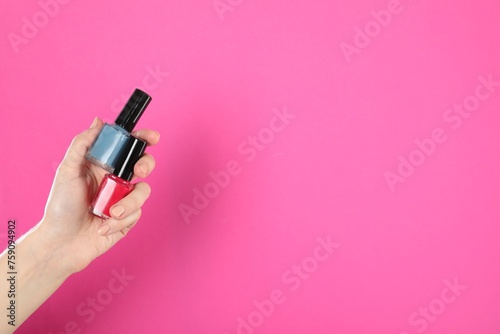 Woman holding nail polishes on pink background, closeup. Space for text