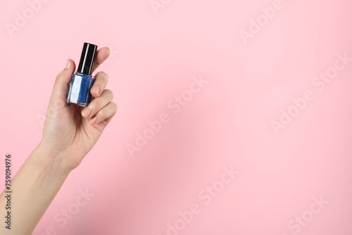 Woman holding nail polish on pink background, closeup. Space for text