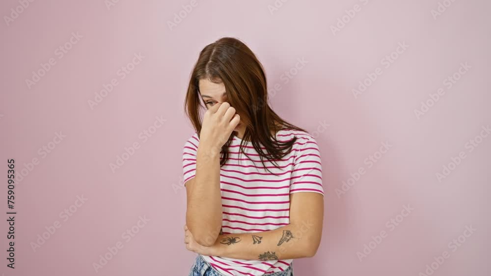Tired young brunette rubs her eyes and nose, battling headache and fatigue. frustrated girl in a stripes tshirt, stressed out over pink isolated background. Tired young brunette rubs her eyes and nose, battling headache and fatigue. frustrated girl in a stripes tshirt, stressed out over pink isolated background.