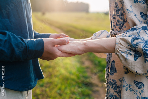 Crop handsome man holding hands of his woman in countryside at sunset photo