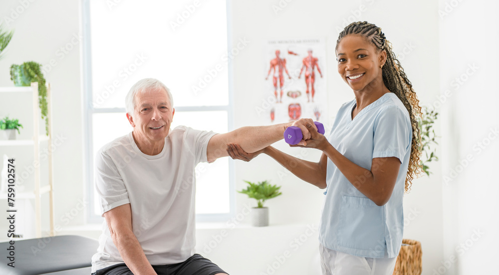 Fototapeta premium Black physiotherapist helping senior man with in clinic. Elderly man undergoing physiotherapy treatment for injury