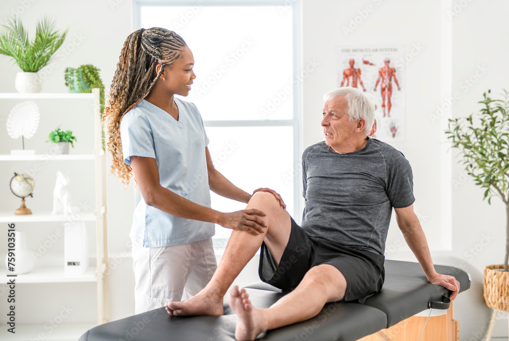 Obraz premium Black physiotherapist helping senior man with in clinic. Elderly man undergoing physiotherapy treatment for injury