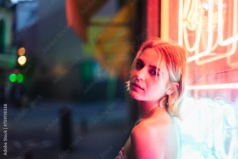 Portrait of a confident young woman leaning on a neon panel at night Portrait of a confident young woman leaning on a neon panel at night
