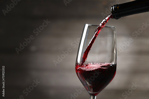 Pouring red wine into glass against gray background, closeup. Space for text