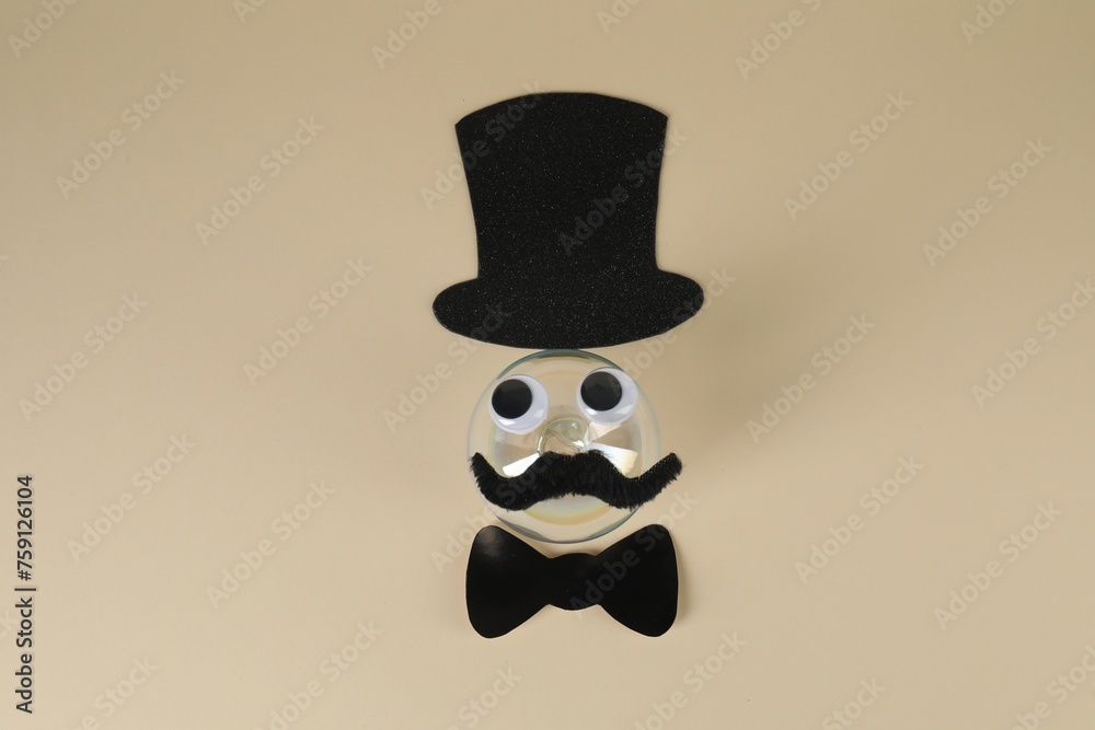 Man's face made of fake mustache, ball, hat, bow tie and eyes on beige background, top view