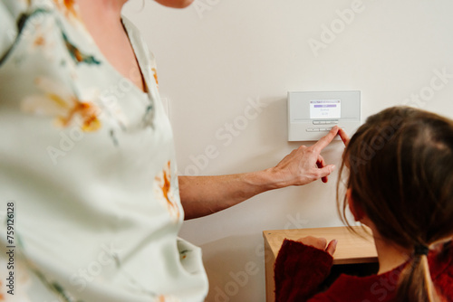 Mother learning child how to use thermostat technology at home photo