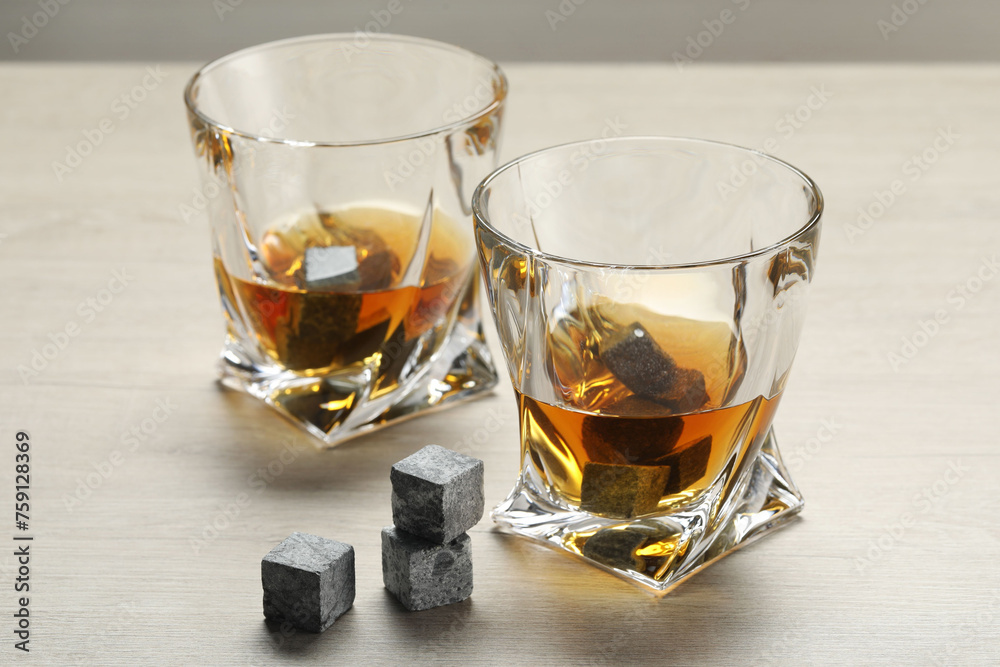 Whiskey stones and drink in glasses on light wooden table, closeup