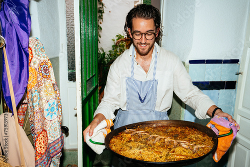 Cheerful man carrying pan with paella at home photo