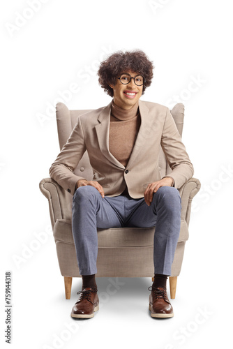 Young man with curly hair and glasses sitting in an armchair and smiling