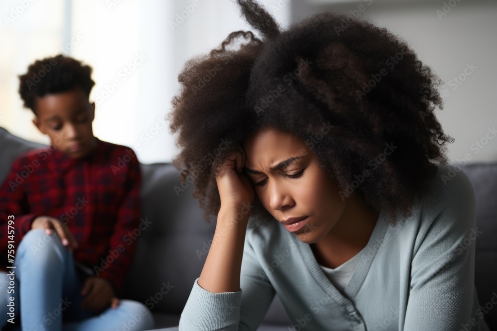 Stressed Single Mother with Child at Home. African American mother with a headache, distressed, with her son in the background. Stressed Single Mother with Child at Home. African American mother with a headache, distressed, with her son in the background.