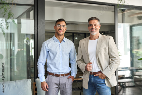 Portrait of two elegant happy confident business men professional executive people partners work team, male company managers looking at camera standing together in corporate office.