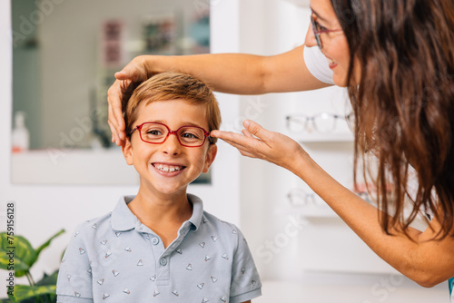 Smiling optician trying on glasses for positive boy photo