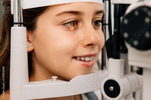 Cheerful girl sitting and looking into eye test machine photo