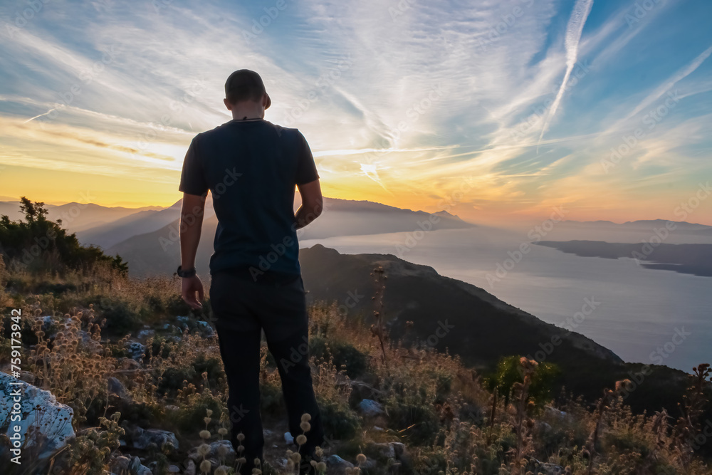 Hiker man with scenic sunrise view from top of mount Kula near Omis, Dinara mountains, Split-Dalmatia, Croatia, Europe. Coastline of Makarska Riviera, Adriatic Sea. Balkans in summer. Biokovo mountain