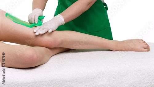 The adhesive tape of wax is removed from the skin on a female thigh lying sideways on table. A depilatory master carefully performs cosmetic hair removal procedure. Showing high skill in beauty salon photo