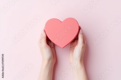 Hands holding a heart-shaped gift box on a pink background.