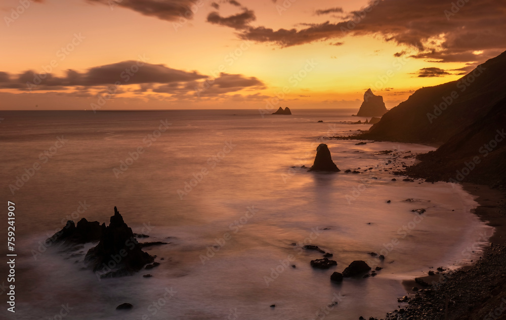 The last light of day illuminates Playa de Benijo with a soft amber glow, highlighting the unique rock formations and tranquil sea The last light of day illuminates Playa de Benijo with a soft amber glow, highlighting the unique rock formations and tranquil sea
