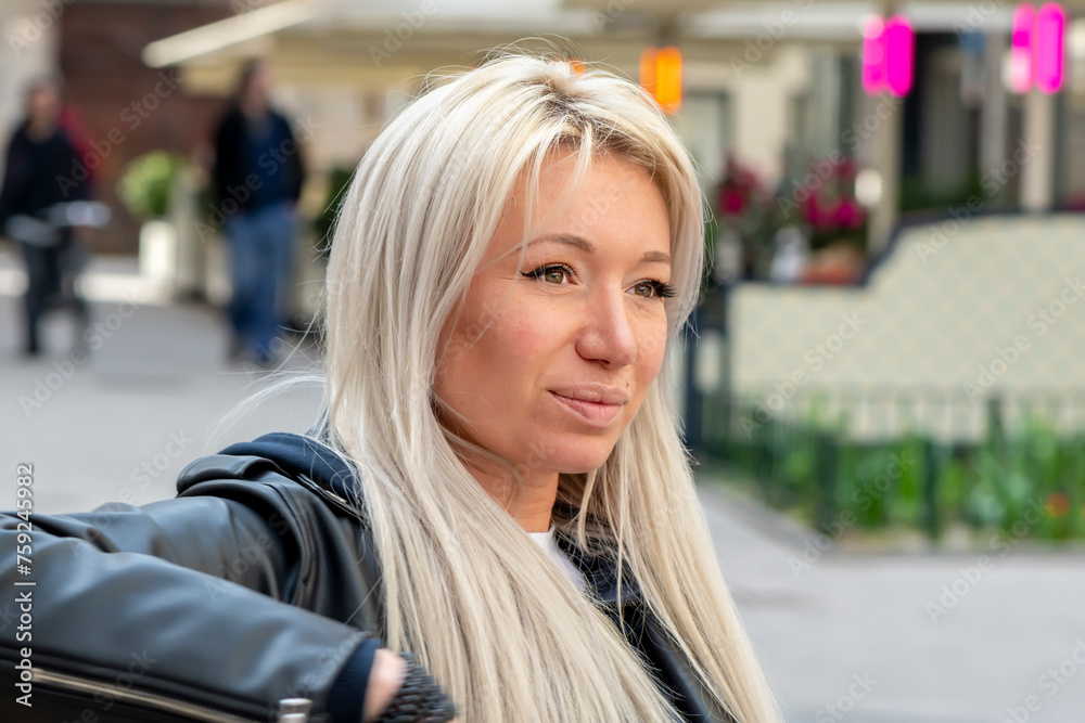 Street portrait of a beautiful blonde woman 35-40 years old against a blurred city background