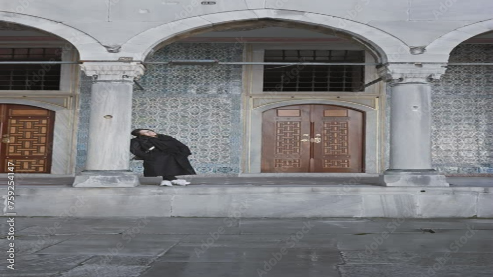 A woman in black stands amidst the historic and ornate architecture of topkapi palace in istanbul, turkey.