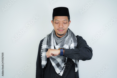 Asian Muslim man wearing Arab turban sorban excited face expression looking at watch, wearing Arabic costume in copy space on isolated background photo