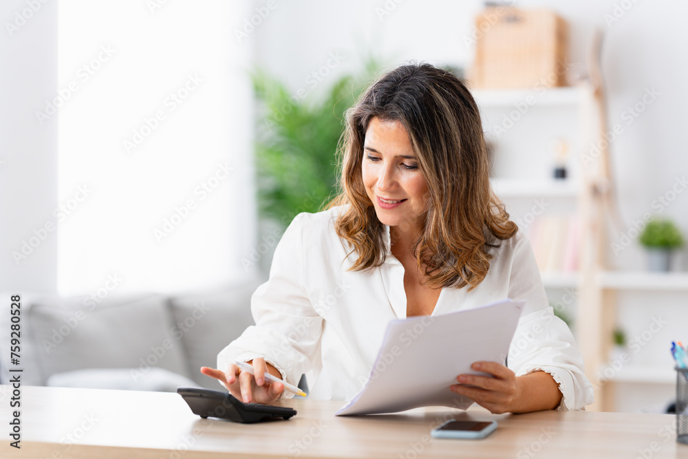 Portrait of a smiling mature woman using calculator to do home finances Portrait of a smiling mature woman using calculator to do home finances