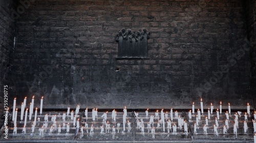 Thin white candles on the soot-blackened exterior wall of a church provide spiritual, warm light at a Catholic pilgrimage site in Germany