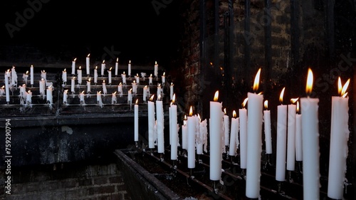 Thin white candles on the soot-blackened exterior wall of a church provide spiritual, warm light at a Catholic pilgrimage site in Germany