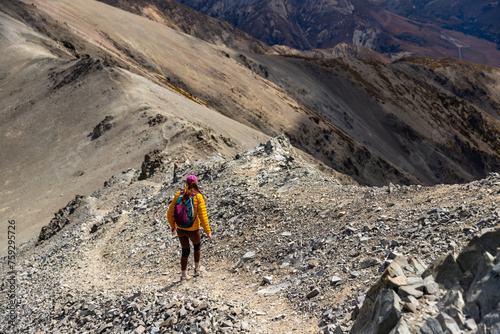 woman walking down a steep rocky mountain ridge of castle hill peak, canterbury, new zealand soth island photo