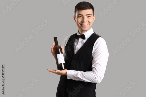 Young sommelier with bottle of wine on grey background