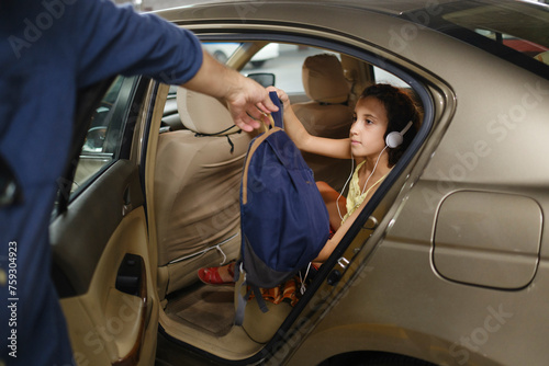 Kid with headphones getting out of car carrying backpack photo