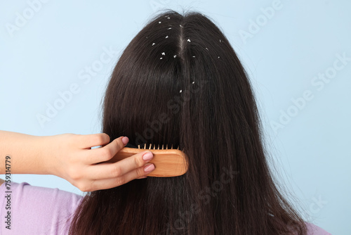 Young woman with dandruff problem combing hair on blue background, back view