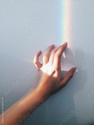 Hand touching wall with beam of light and rainbow reflection