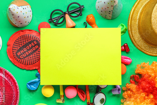 Blank card with whoopee cushion, funny glasses and party decor on green background. April Fools Day celebration
