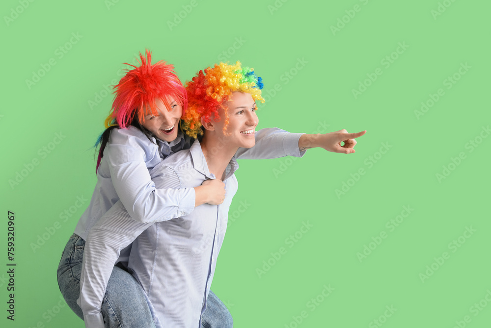 Business colleagues in funny wigs pointing at something on green background. April Fools' Day celebration Business colleagues in funny wigs pointing at something on green background. April Fools' Day celebration