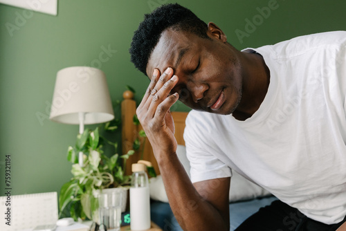 A man sitting in bed and rubbing his forehead photo