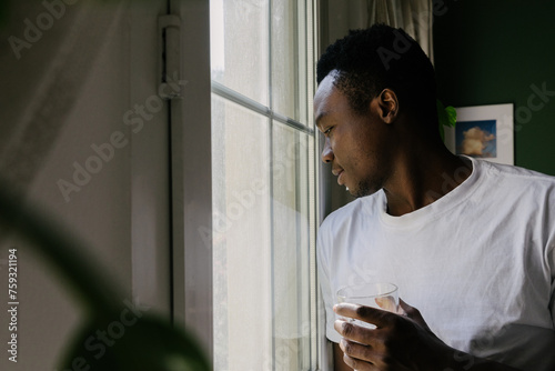 A man standing by the window with a glass of water. photo